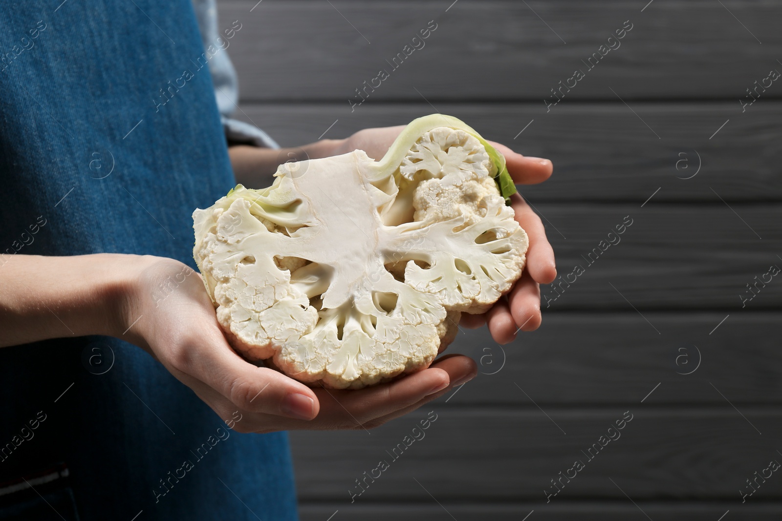 Photo of Woman holding fresh cauliflower against black wooden wall, closeup