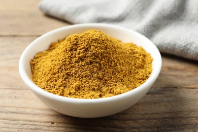 Photo of Dry curry powder in bowl on wooden table, closeup