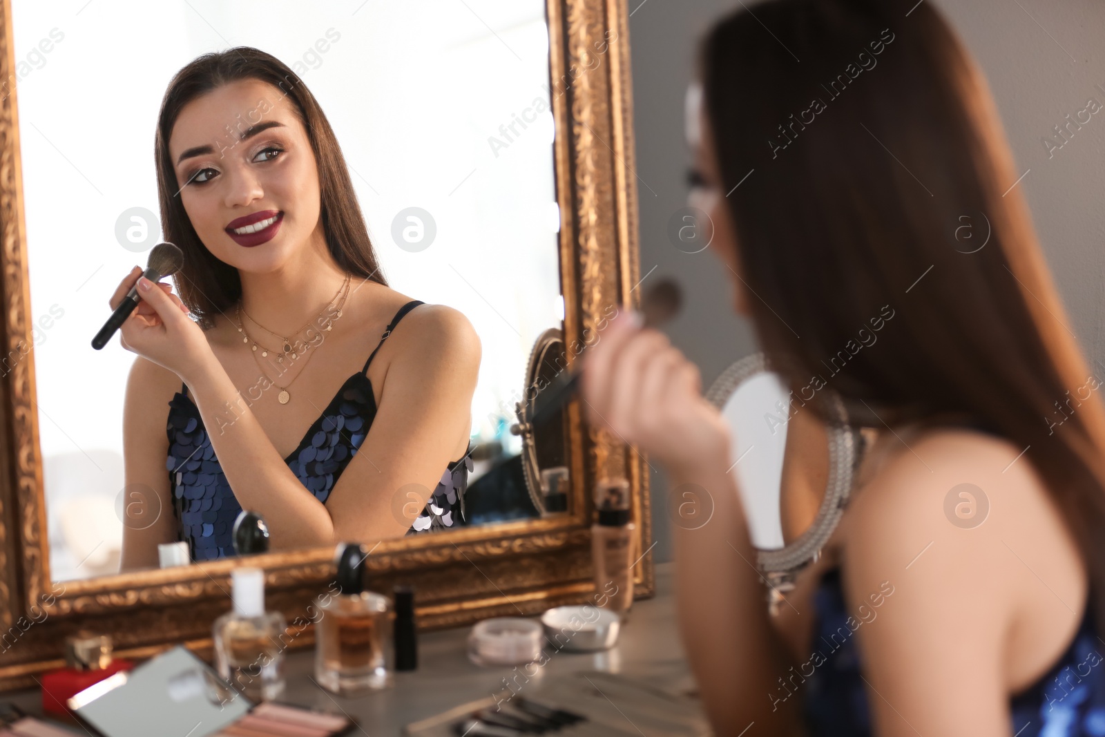 Photo of Portrait of beautiful woman applying makeup near mirror indoors