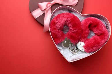 Photo of Gift box with furry handcuffs on red background, top view. Space for text