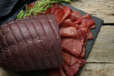 Photo of Tasty bresaola and rosemary on wooden table, top view