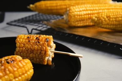 Photo of Ceramic plate with grilled corn cobs on light table, closeup