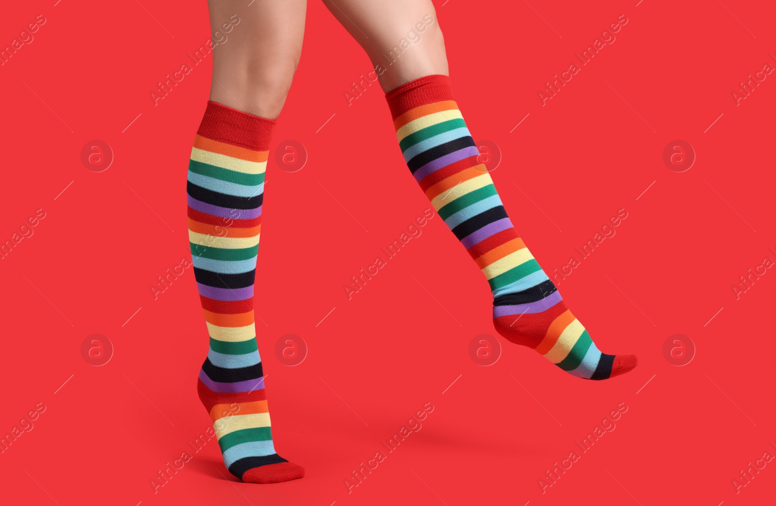 Photo of Woman in stylish rainbow socks on red background, closeup