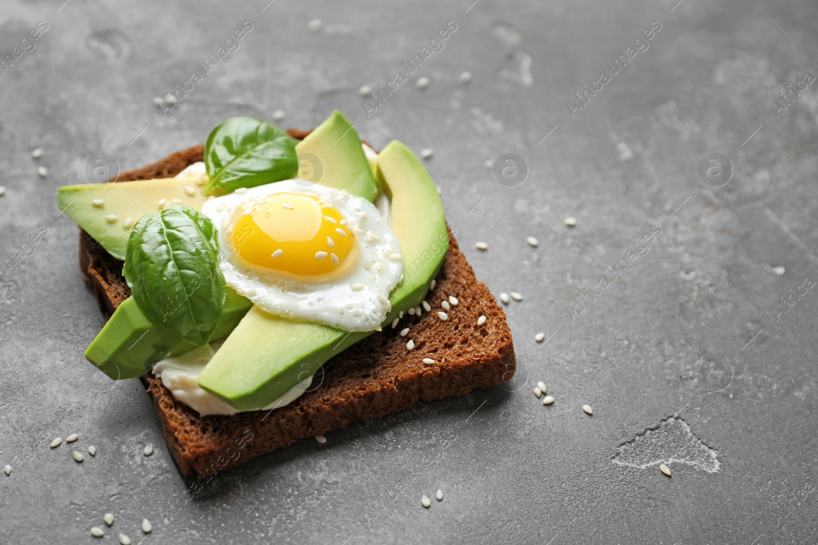 Photo of Toast bread with cream cheese, avocado and fried egg on dark background, closeup