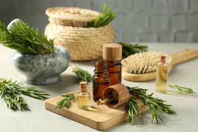 Essential oils in bottles and rosemary on light gray table, closeup