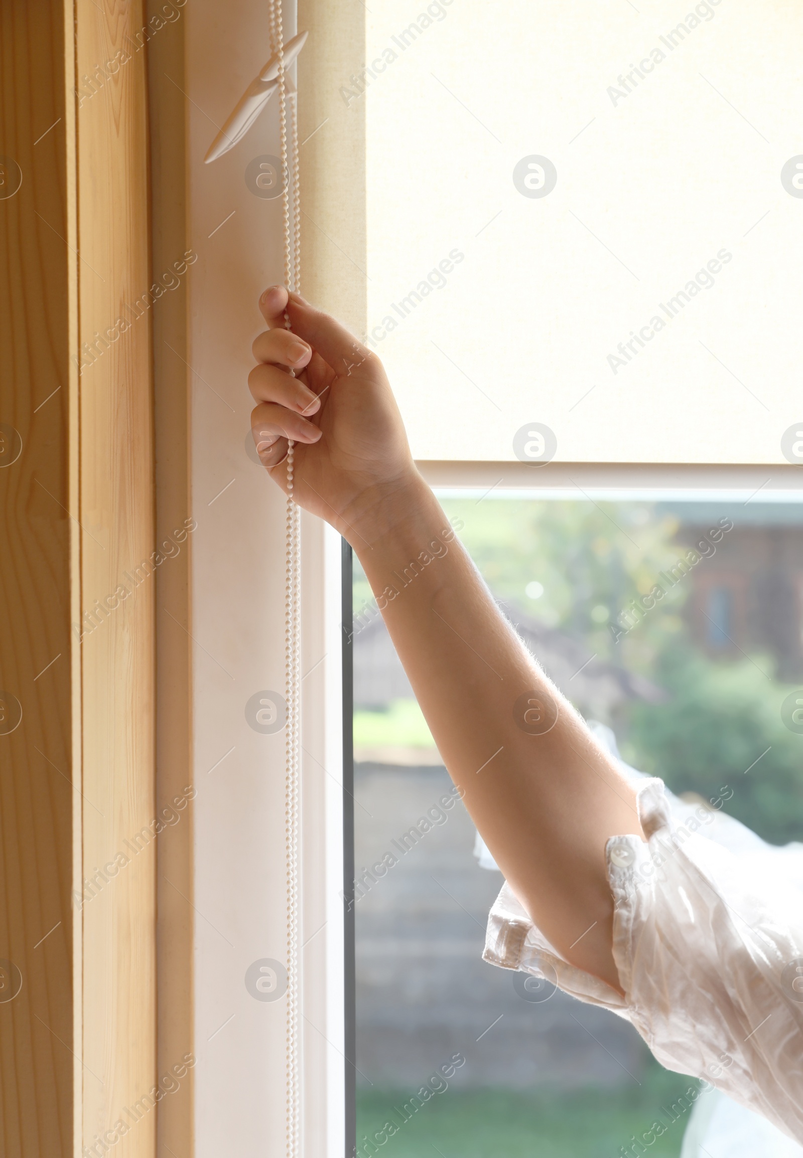 Photo of Young woman opening roller curtains at home, closeup