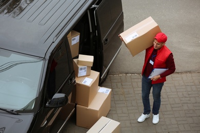 Courier with clipboard and parcel near delivery van outdoors, above view