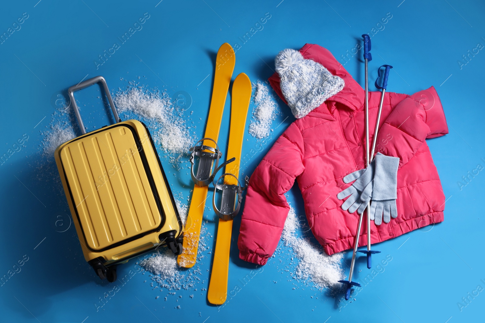 Photo of Suitcase with warm clothes and skis on light blue background, flat lay. Winter vacation