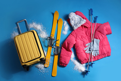 Suitcase with warm clothes and skis on light blue background, flat lay. Winter vacation