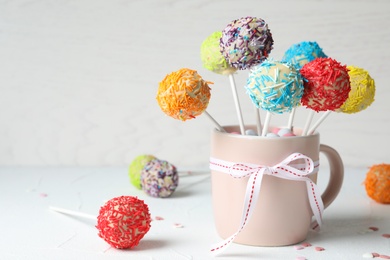 Cup with bow and yummy colorful cake pops on table. Space for text