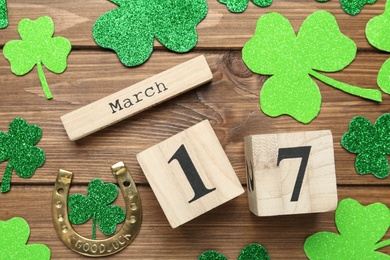 Photo of Decorative clover leaves, horseshoe and block calendar on wooden background, flat lay. St. Patrick's Day celebration