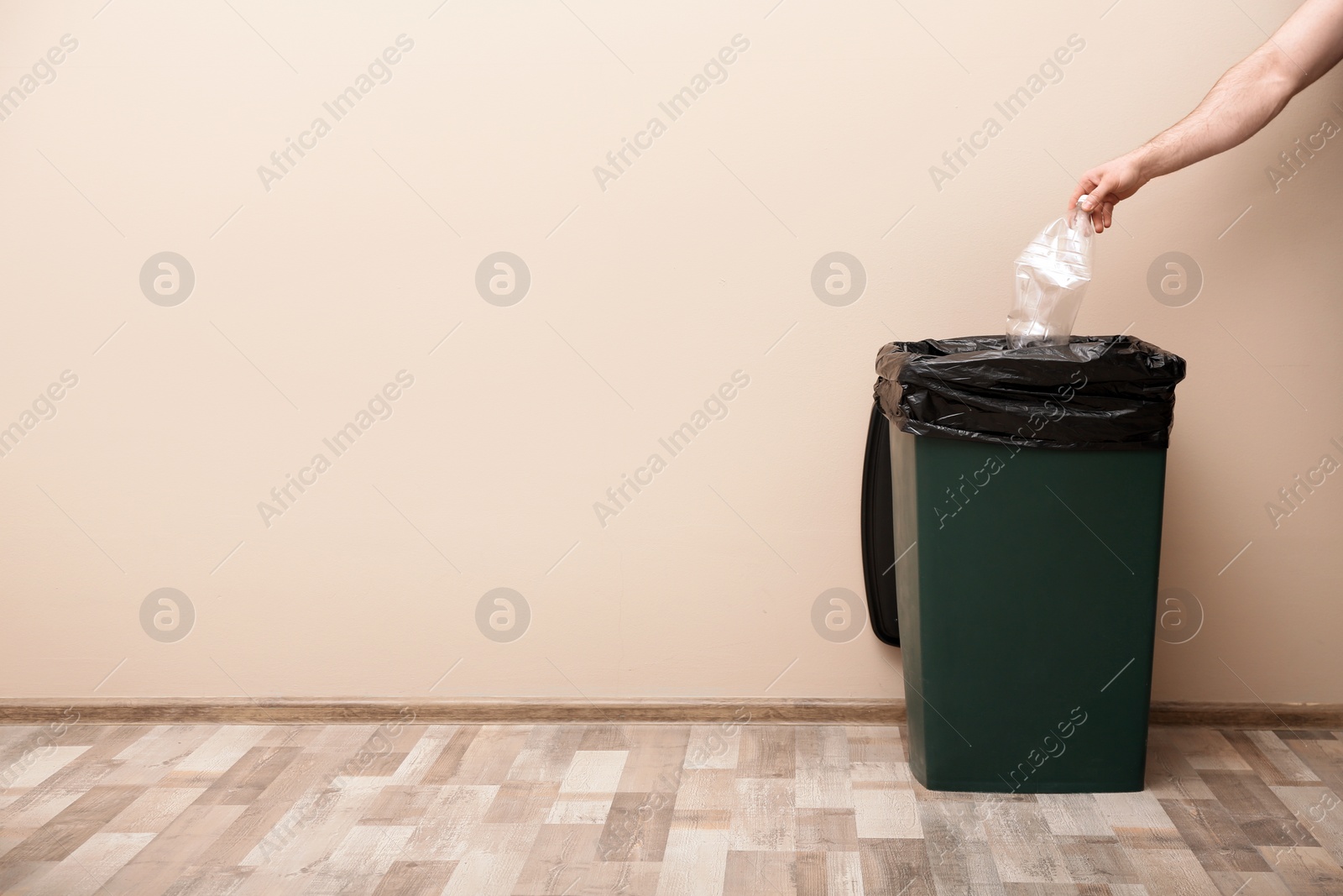 Photo of Young woman throwing plastic bottle in trash bin indoors, space for text. Waste recycling