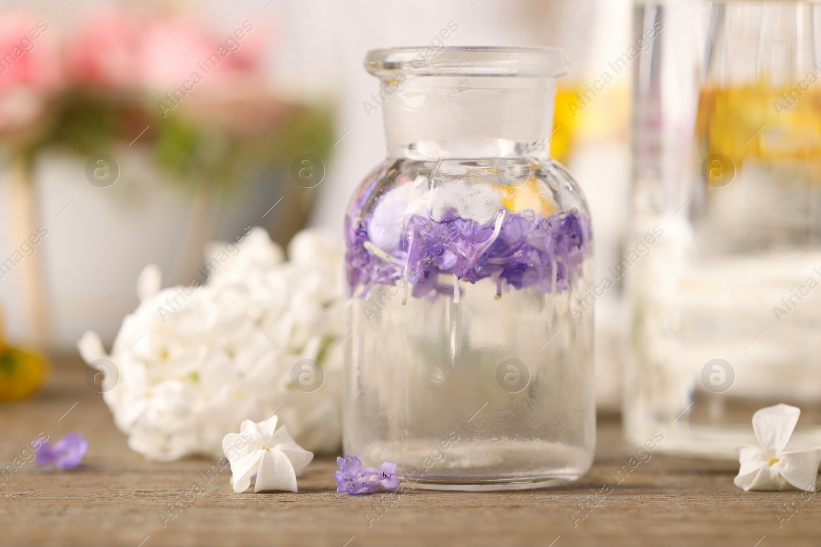 Photo of Apothecary bottle with flowers on wooden table in laboratory, closeup. Extracting essential oil for perfumery and cosmetics