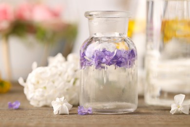 Photo of Apothecary bottle with flowers on wooden table in laboratory, closeup. Extracting essential oil for perfumery and cosmetics