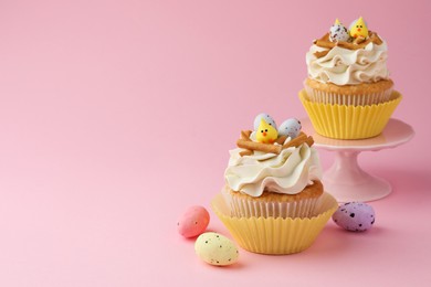 Photo of Tasty Easter cupcakes with vanilla cream and candies on pink background, space for text