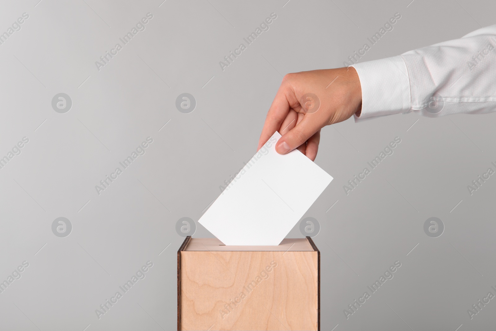 Photo of Man putting his vote into ballot box on light grey background, closeup