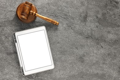 Modern tablet and gavel on gray textured table, flat lay. Space for text