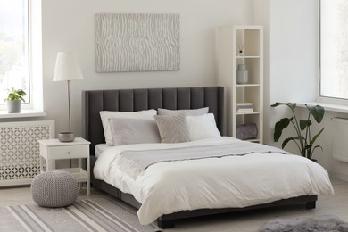 Photo of Stylish light bedroom interior with large comfortable bed, shelving unit and bedside table