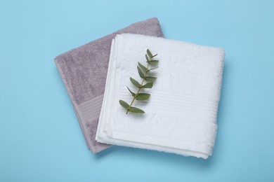 Folded terry towels and eucalyptus branch on light blue background, flat lay
