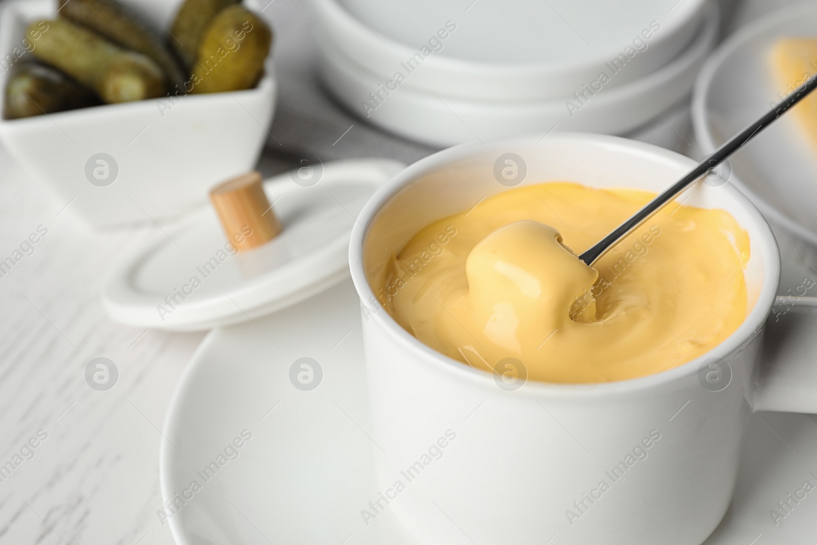 Photo of Pot of tasty cheese fondue and fork with bread on white wooden table