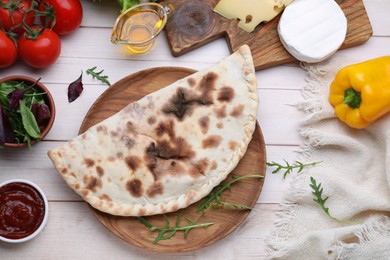 Photo of Delicious calzone and products on light wooden table, flat lay