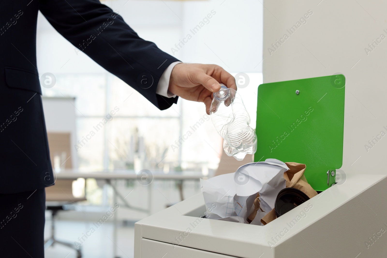 Photo of Man putting used plastic bottle into trash bin in office, closeup. Waste recycling