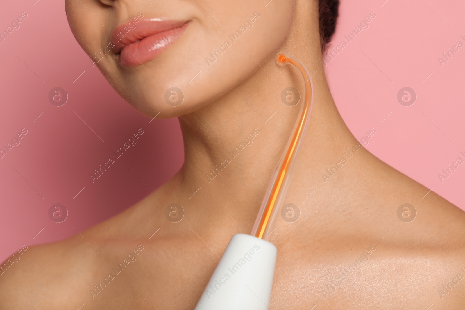 Photo of Woman using high frequency darsonval device on pink background, closeup