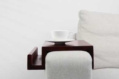 Cup of coffee on sofa with wooden armrest table indoors. Interior element