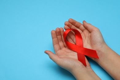 Photo of Little girl holding red ribbon on blue background, closeup with space for text. AIDS disease awareness