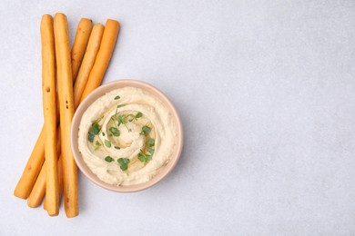 Photo of Delicious hummus with grissini sticks on light grey table, flat lay. Space for text