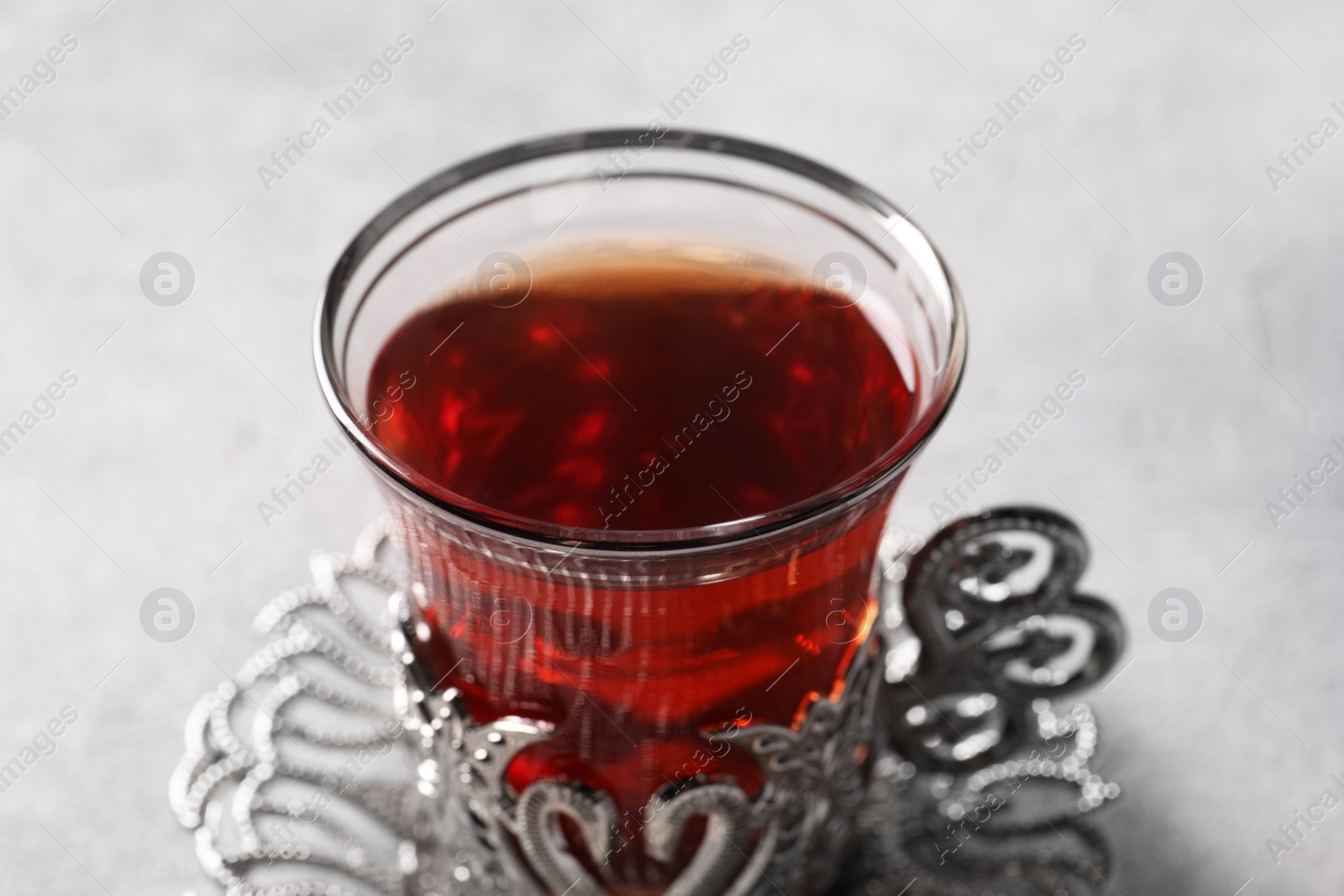 Photo of Glass of traditional Turkish tea in vintage holder on light grey table, closeup