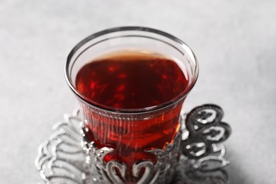 Glass of traditional Turkish tea in vintage holder on light grey table, closeup