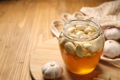 Photo of Honey with garlic in glass jar on wooden table. Space for text