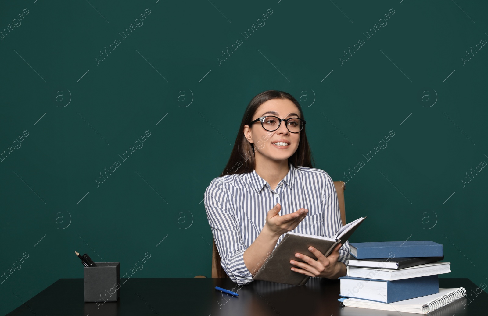 Photo of Portrait of young teacher at table against green background. Space for text