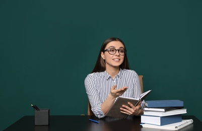 Portrait of young teacher at table against green background. Space for text