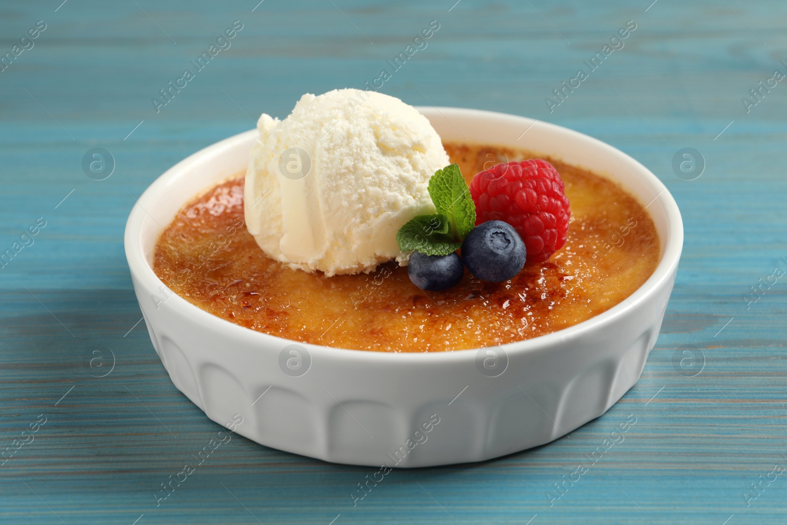 Photo of Delicious creme brulee with scoop of ice cream, fresh berries and mint on light blue wooden table, closeup