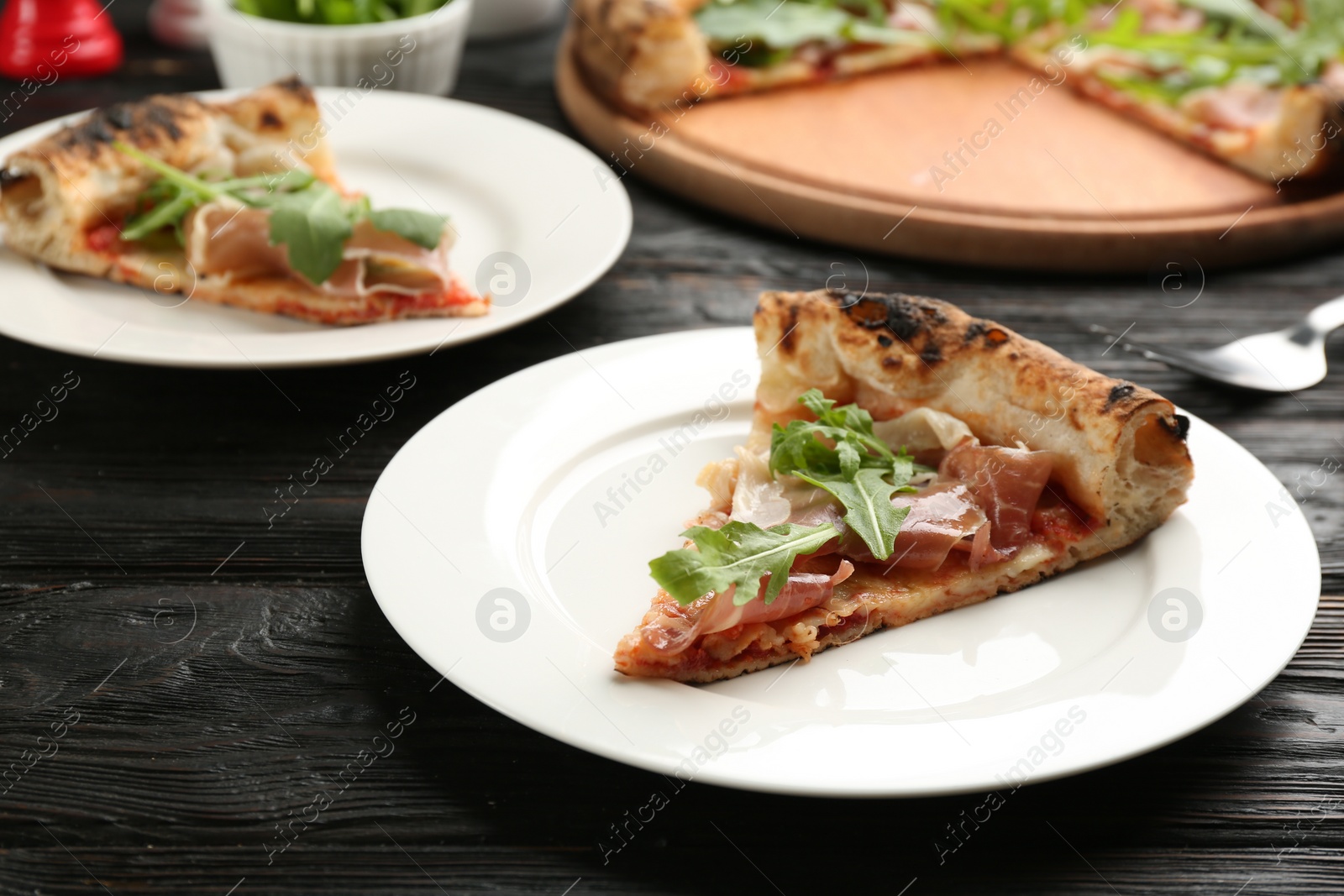 Photo of Slice of tasty pizza with meat and arugula on black wooden table, closeup