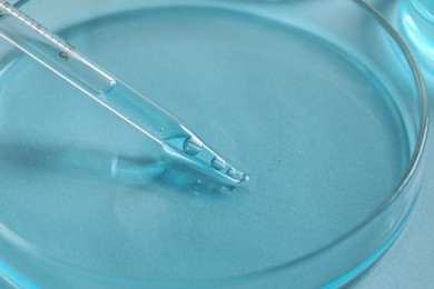 Photo of Dripping liquid from pipette into petri dish at light blue table, closeup. Laboratory analysis
