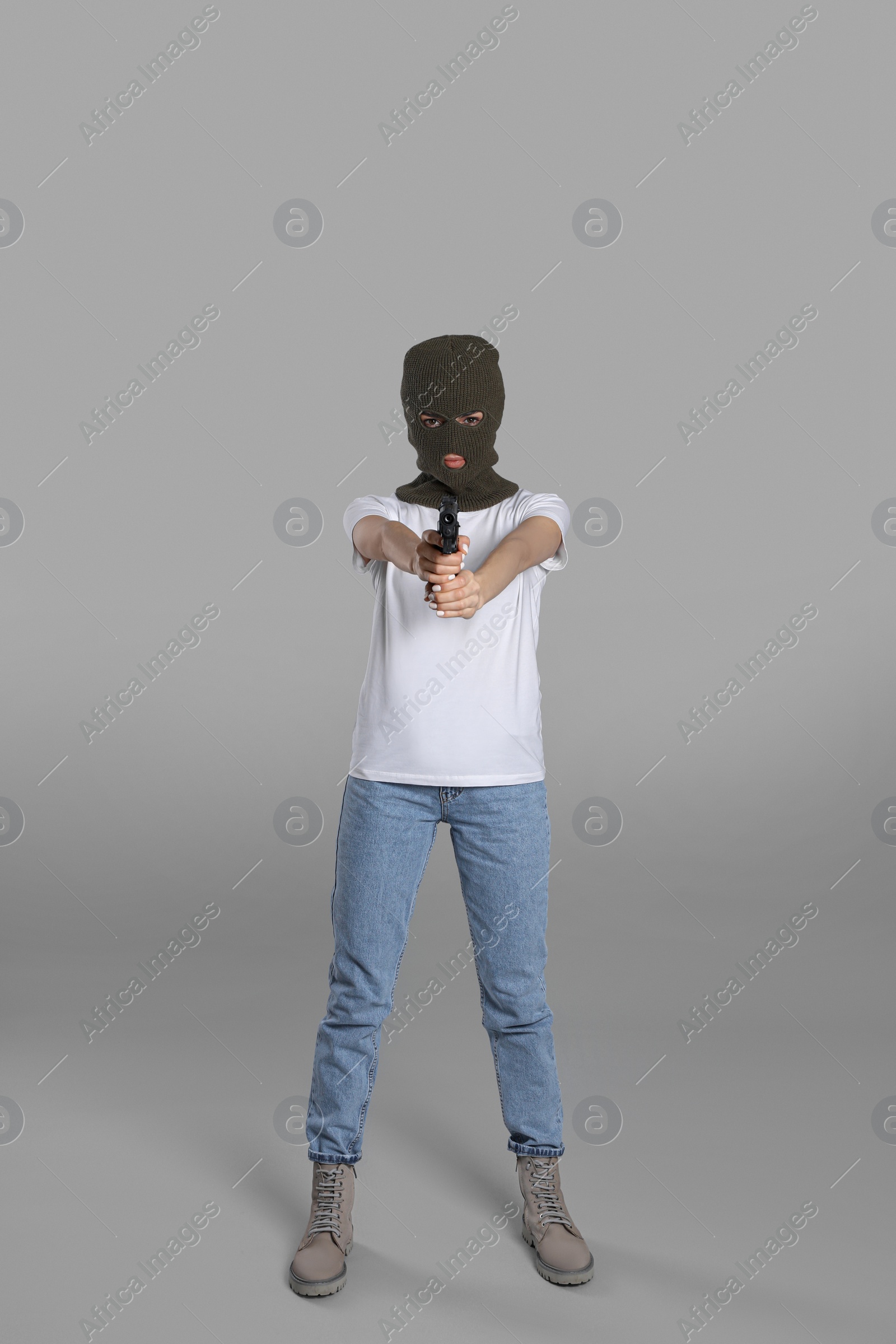 Photo of Woman wearing knitted balaclava with gun on grey background