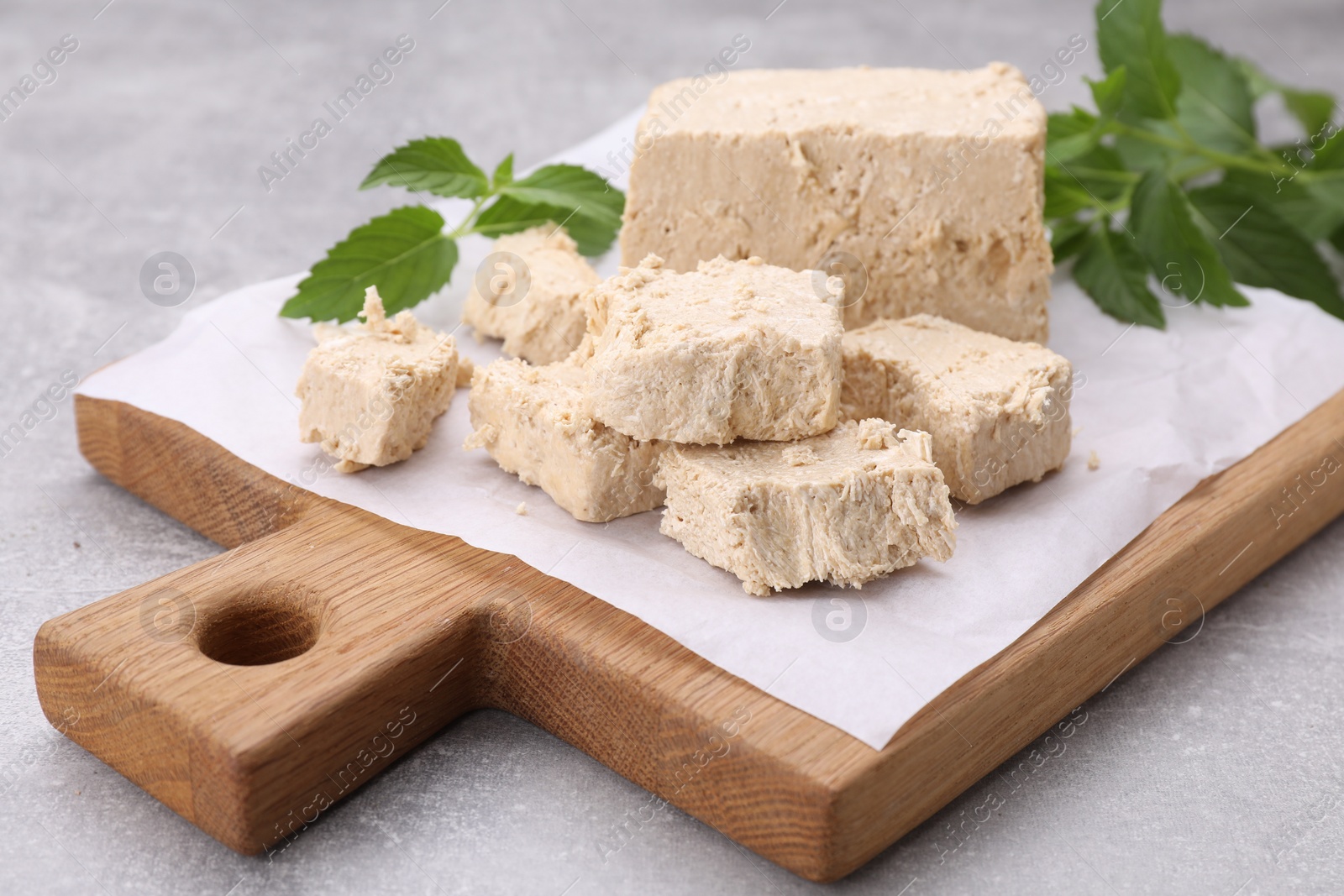Photo of Pieces of tasty halva and mint leaves on light grey table, closeup