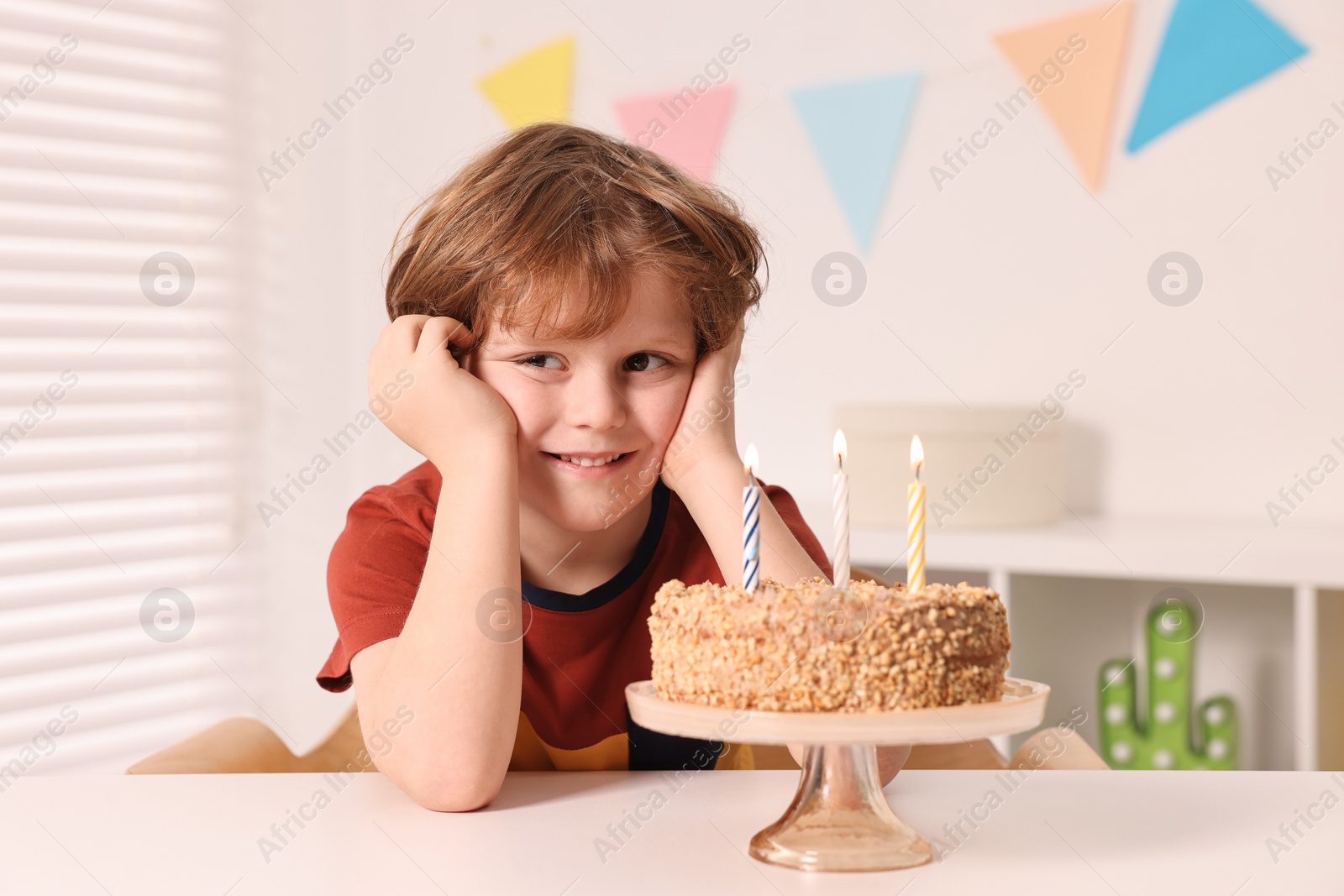 Photo of Cute boy with birthday cake at table indoors