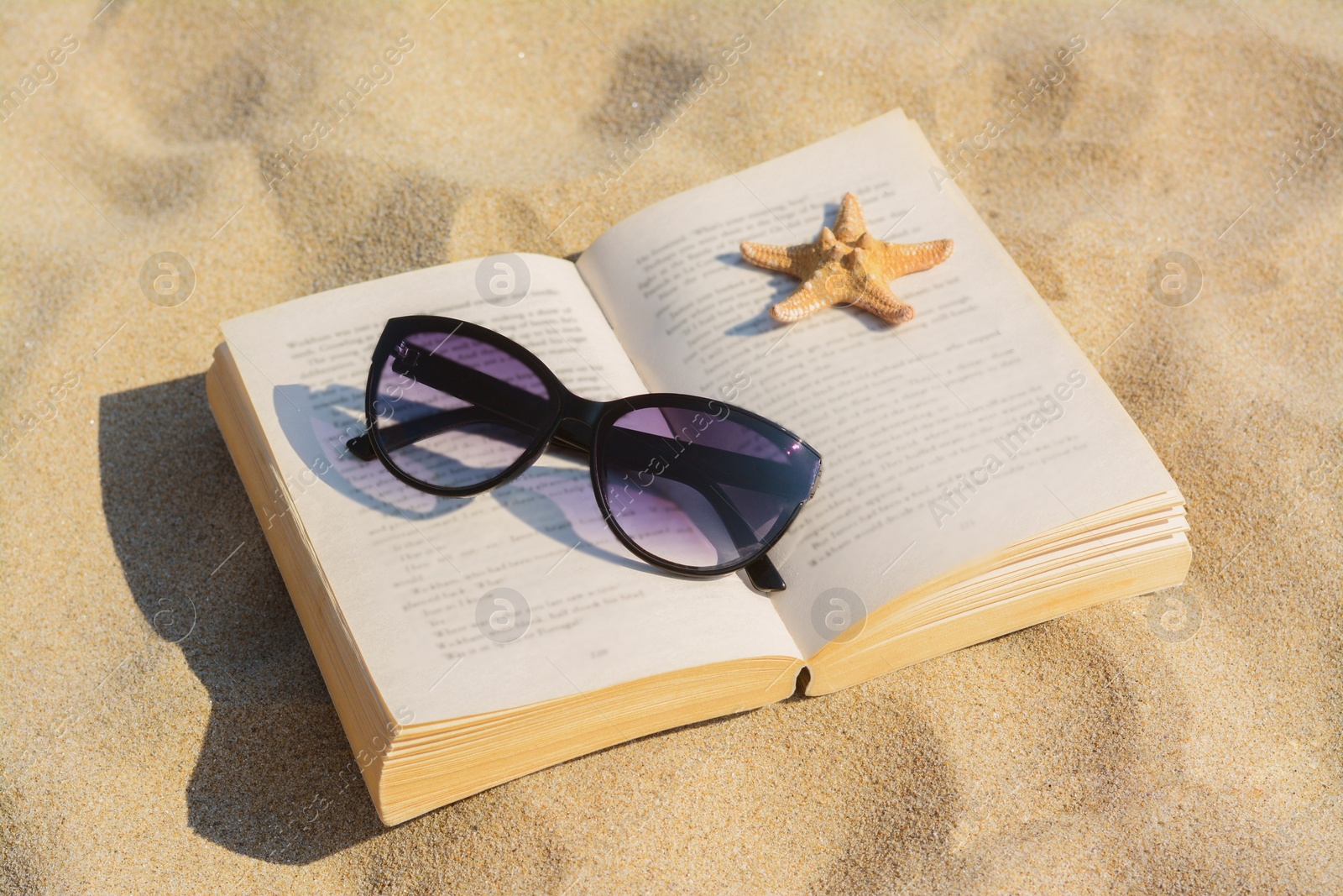 Photo of Beautiful sunglasses, book and starfish on sand