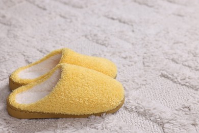 Photo of Yellow soft slippers on light carpet, closeup. Space for text