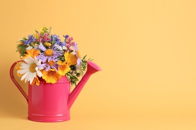 Photo of Pink watering can with beautiful flowers on yellow background, space for text