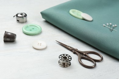 Photo of Composition with different sewing supplies and fabric on white wooden table