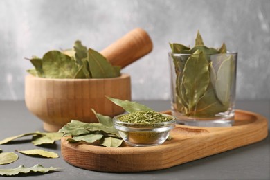 Photo of Whole and ground dry bay leaves on grey table, closeup