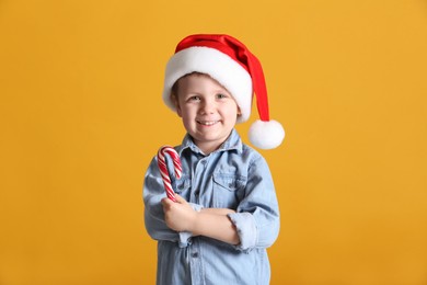 Photo of Cute little boy in Santa Claus hat holding candy cane on yellow background