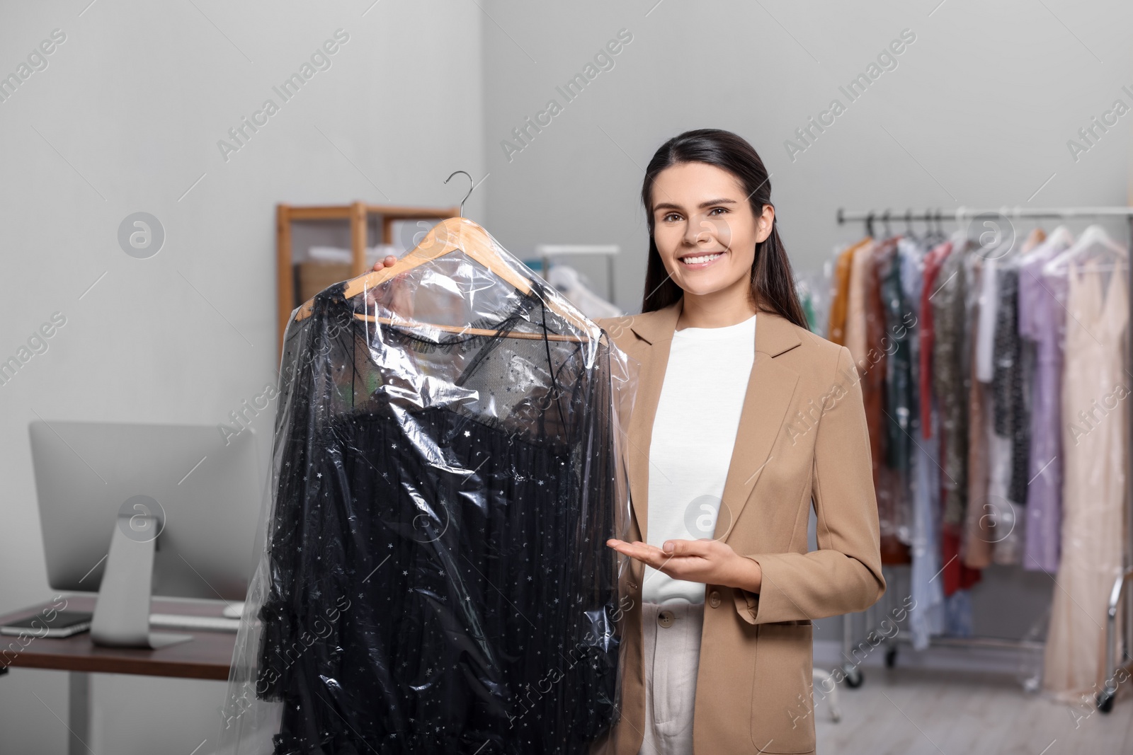 Photo of Dry-cleaning service. Happy woman holding hanger with dress in plastic bag indoors