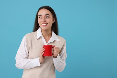 Happy young woman holding red ceramic mug on light blue background, space for text