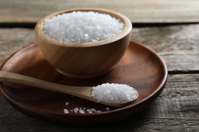 Organic salt in bowl and spoon on wooden table, closeup